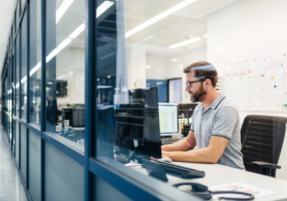 Technician working in control room of a factory looking on computer monitors and tracking production