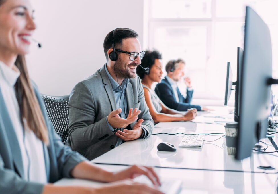 Shot of call center operators working in the office. Call center agent working with his colleagues in modern office. Smiling handsome businessman working in call center.