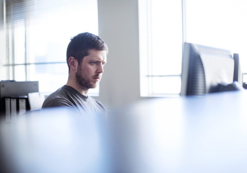 A photo of businessman using computer in cubicle in office. Concentrated male executive is working on desktop PC. Confident male professional is in brightly lit office.