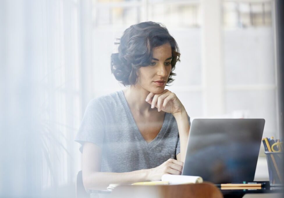 Beautiful young businesswoman with hand on chin using laptop in office