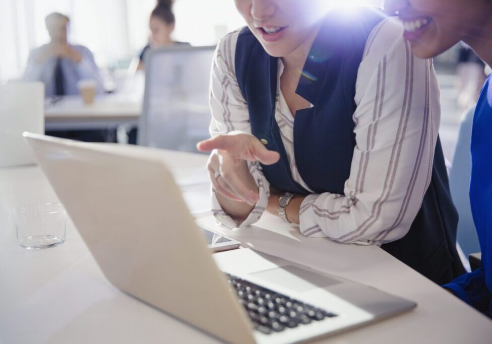 Businesswomen talking, working at laptop in office meeting
